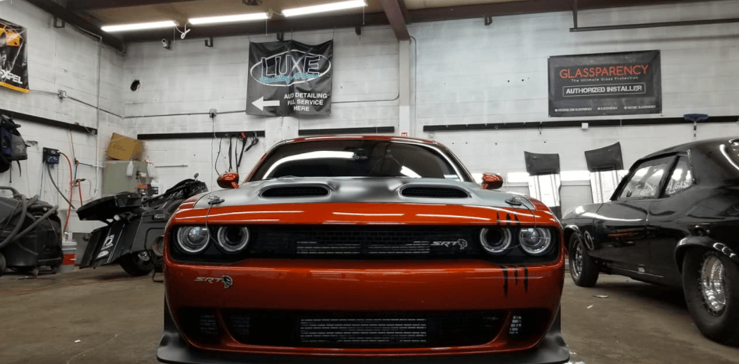 Orange Dodge Challenger in a garage, a black car is to the right.