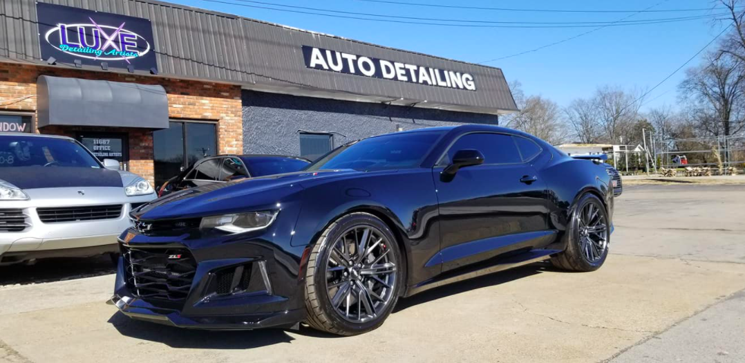 Black Chevy Camaro parked in front of an auto detailing shop.