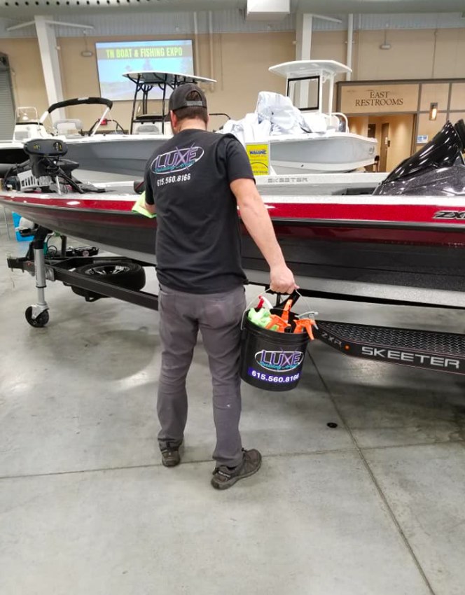 Man cleaning a boat, holding a bucket. Boat is in a showroom.