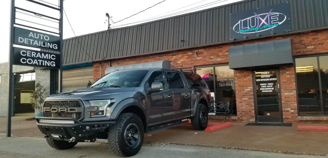 A gray Ford Raptor truck parked outside a auto detailing shop.
