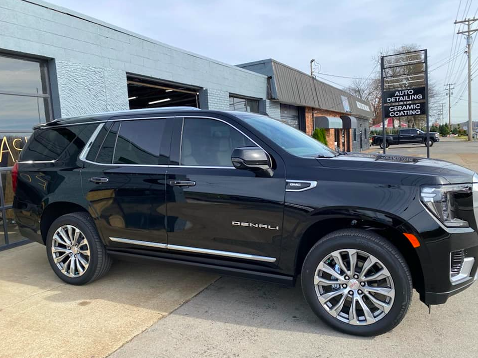 Black GMC Yukon Denali SUV parked outside a business, under a bright sky.