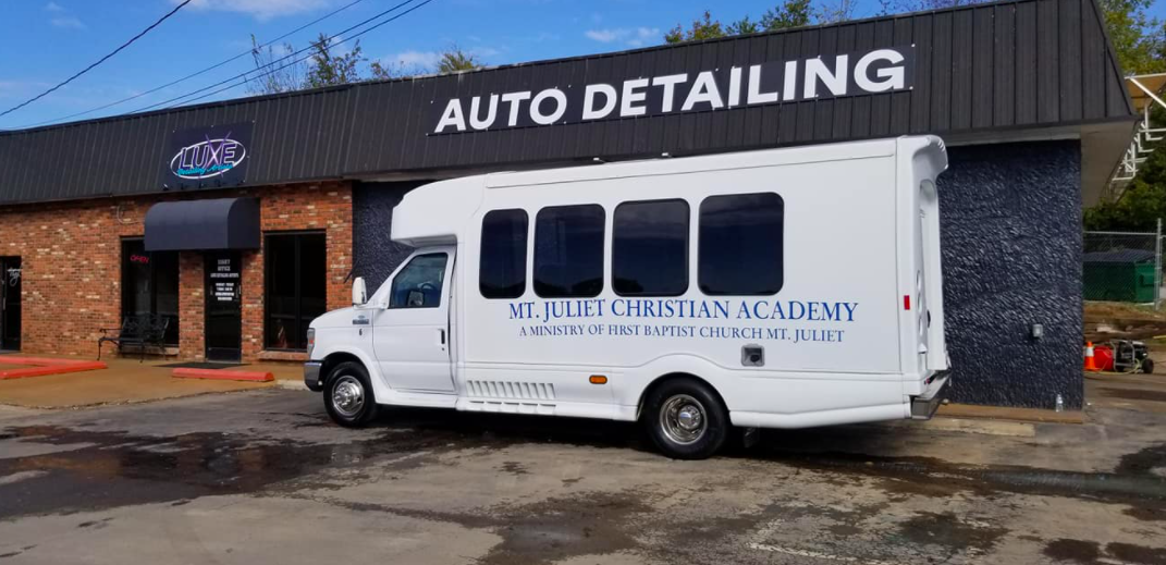 A white bus parked outside an auto detailing shop. The bus is marked with 