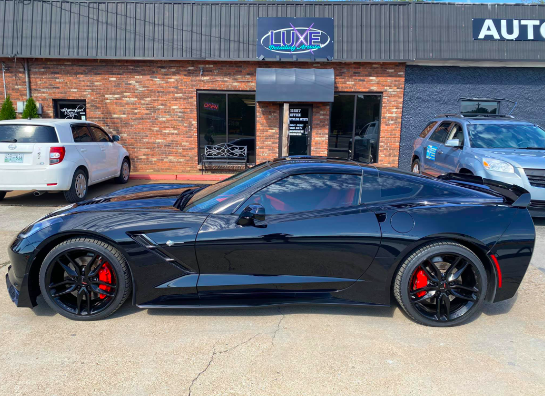 Black sports car parked in front of Luxe Auto dealership with red brake calipers.
