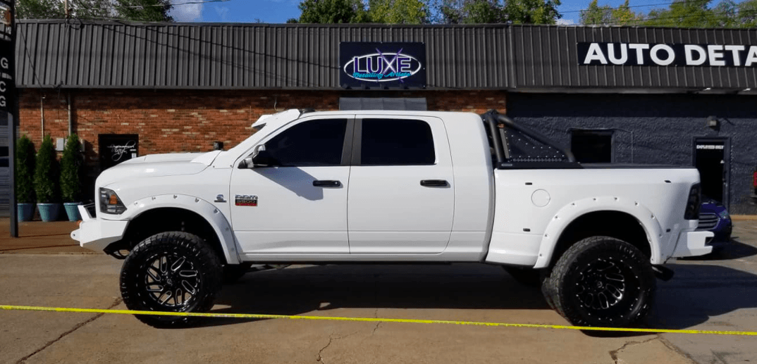 White lifted pickup truck parked outside an auto detailing business.