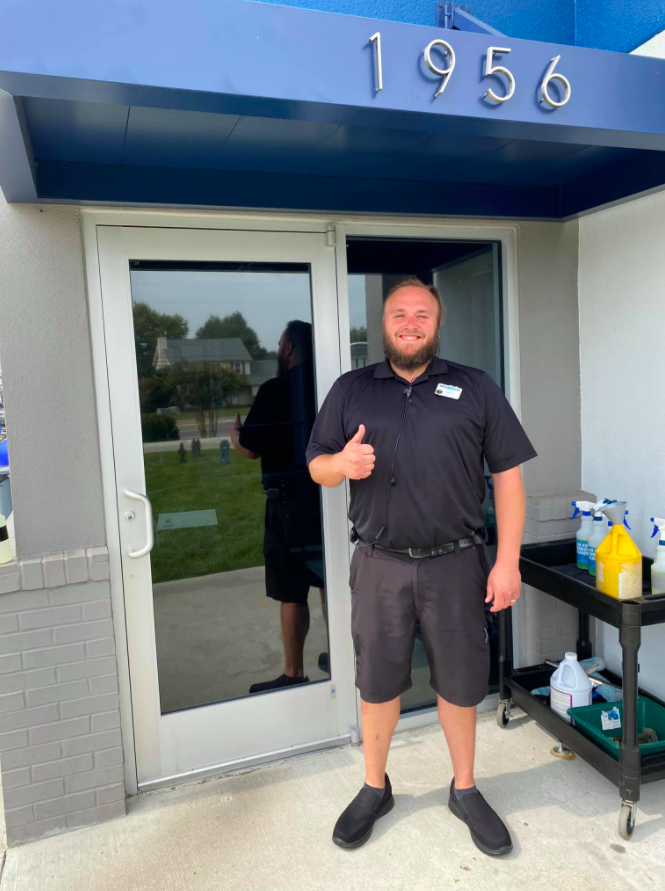 Man in black uniform giving thumbs up in front of building with 