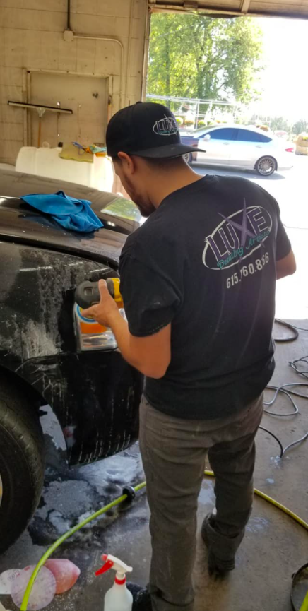 Man in a black t-shirt and hat working on a car in a garage.