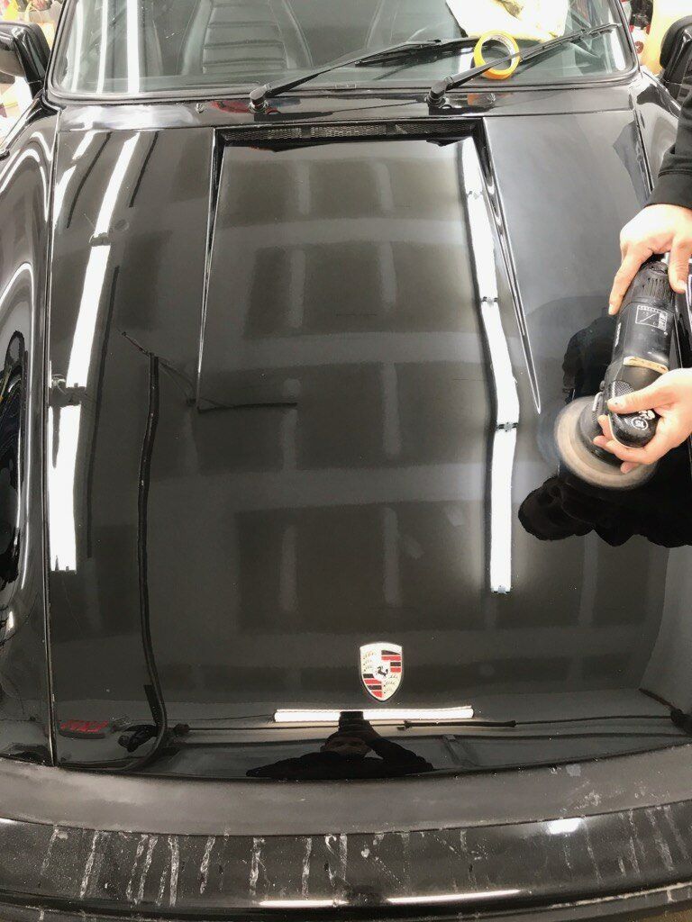 Black car hood being polished, with a person holding a polisher.