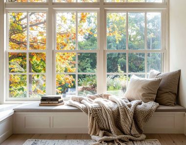 A cozy window nook with neutral pillows and a knitted blanket