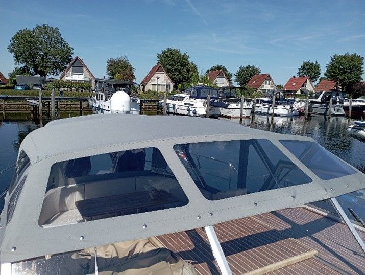 Een boot met een doorzichtige kap ligt aangemeerd in een jachthaven