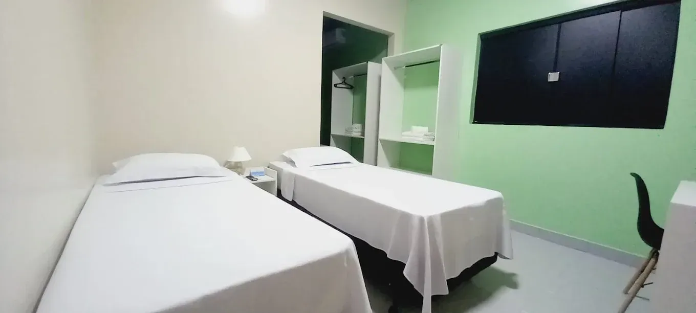 Um quarto com duas camas, uma escrivaninha e uma janela.