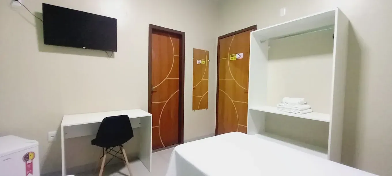 Um quarto com uma cama, escrivaninha, cadeira e televisão.