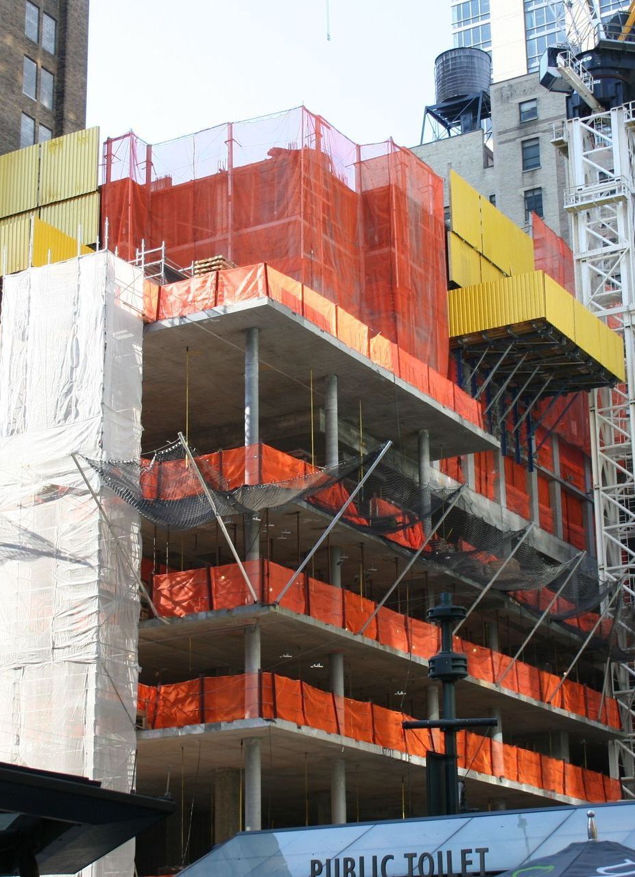 Construction site of a building with orange safety netting, exposed concrete floors, and a crane.