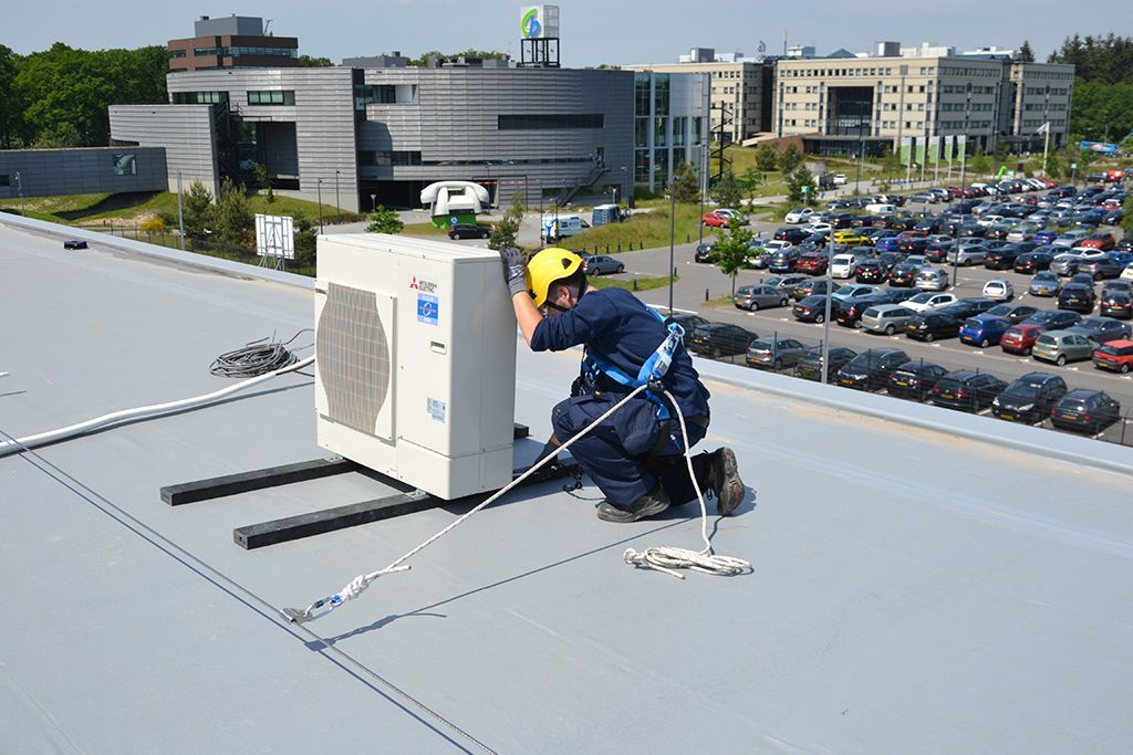 A man is working on an air conditioner on the roof of a building.