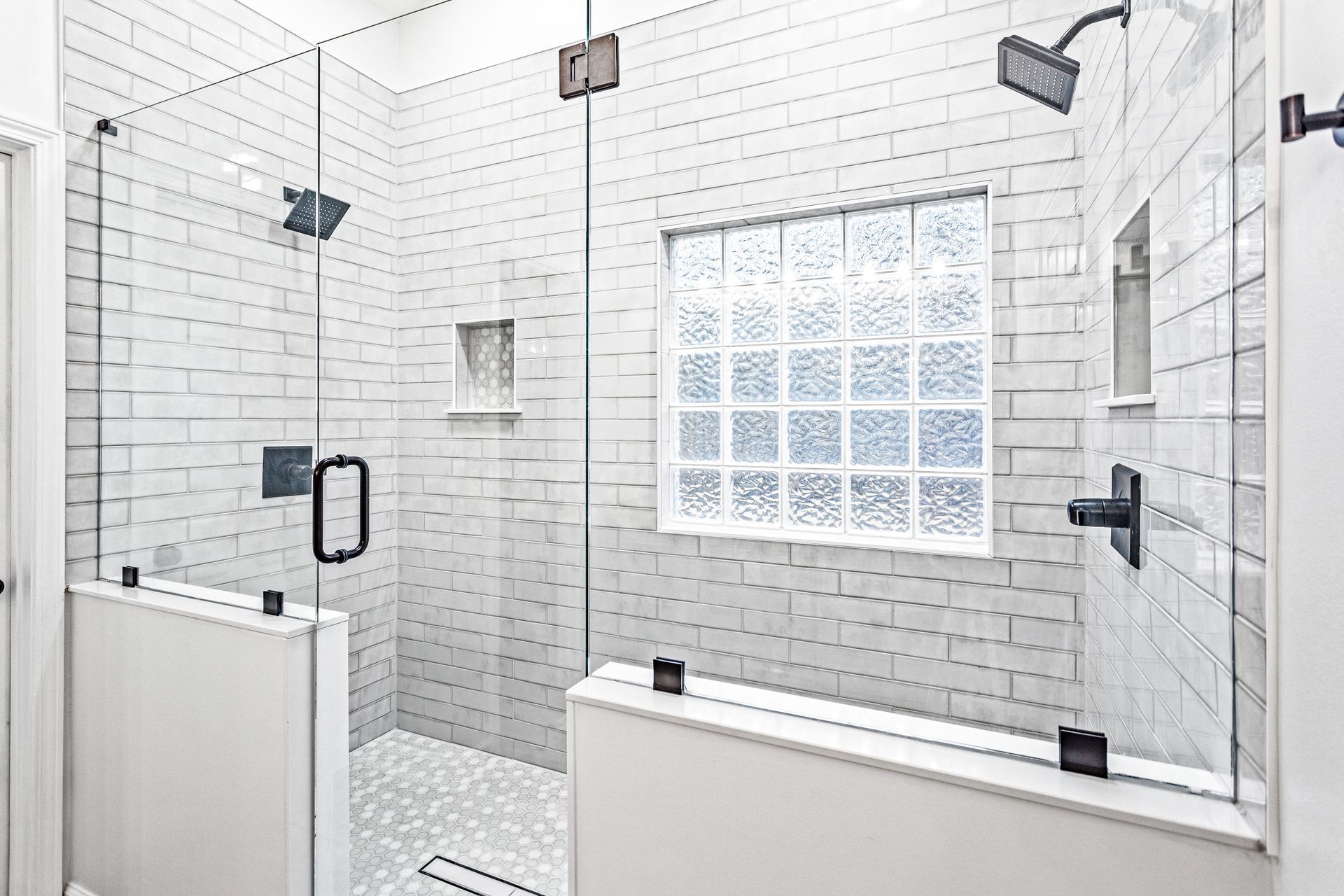 A bathroom with white tiles and a walk in shower with a glass door.
