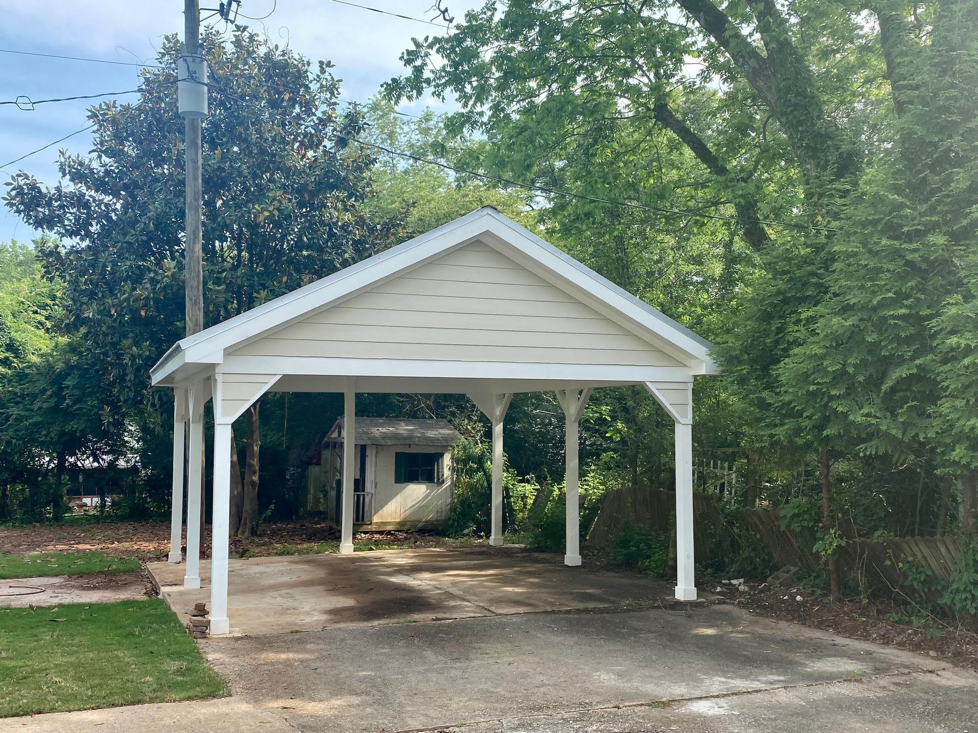 A white carport is in the middle of a driveway surrounded by trees.