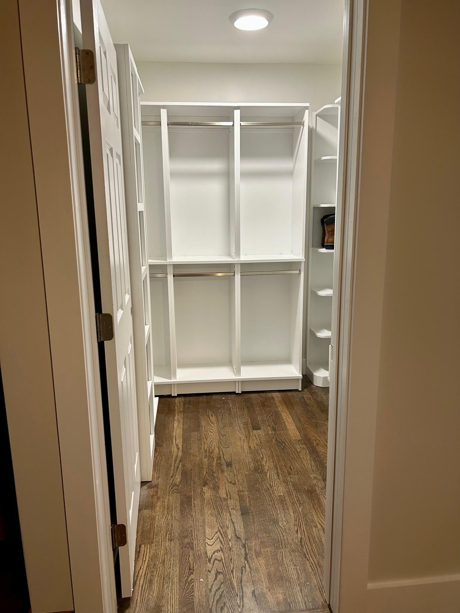 A walk in closet with wooden floors and white shelves.