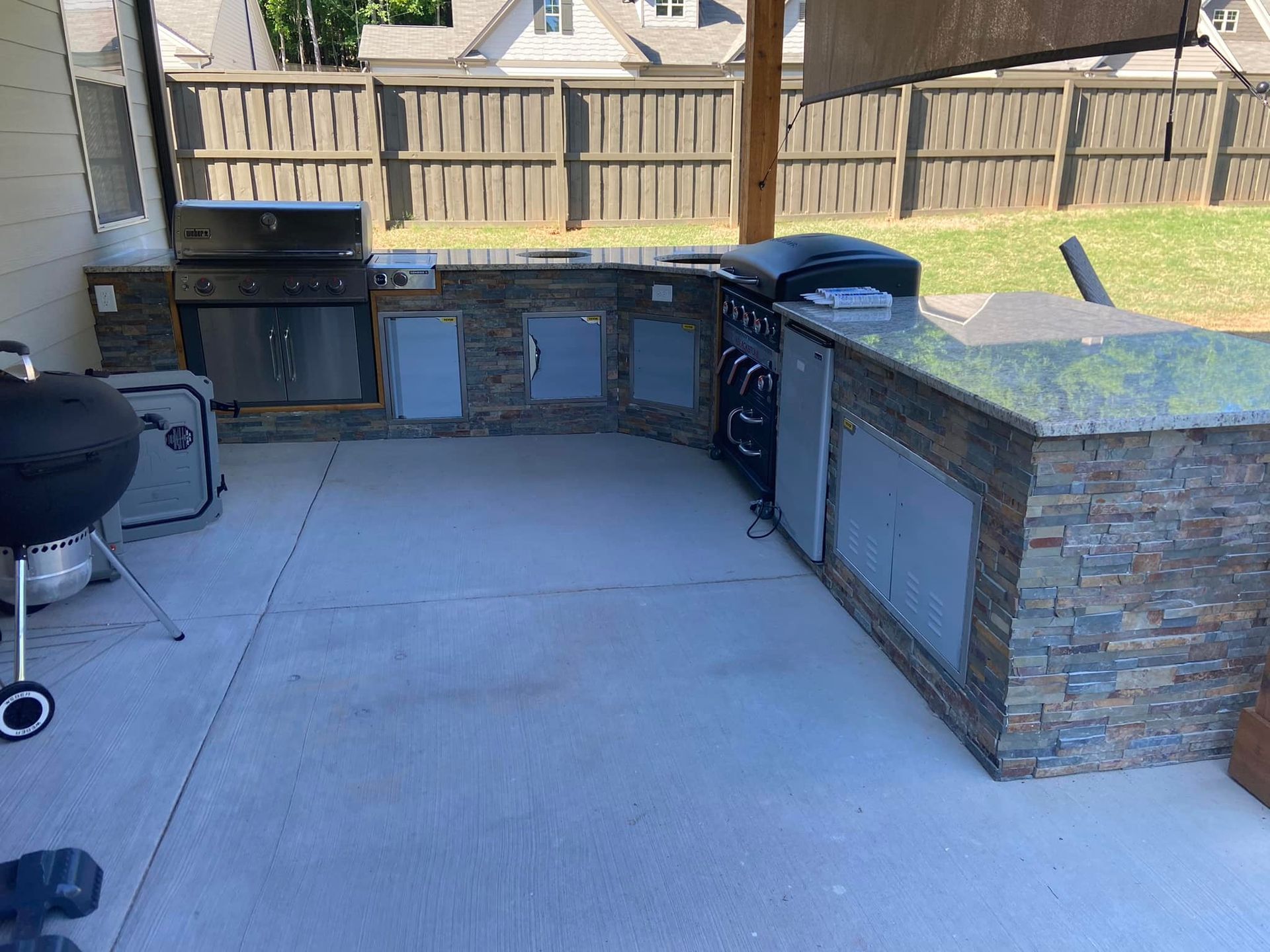 A large outdoor kitchen with a grill and a fence in the background.