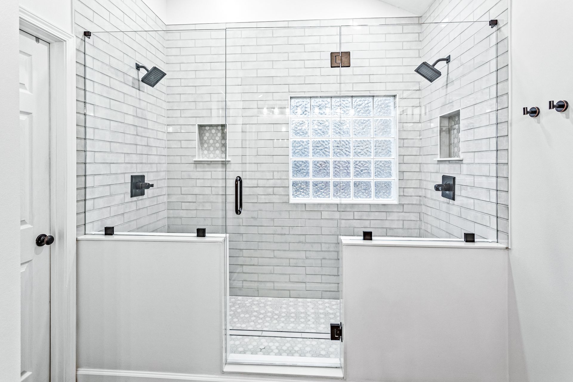 A bathroom with white tiles and a walk in shower with a glass door.