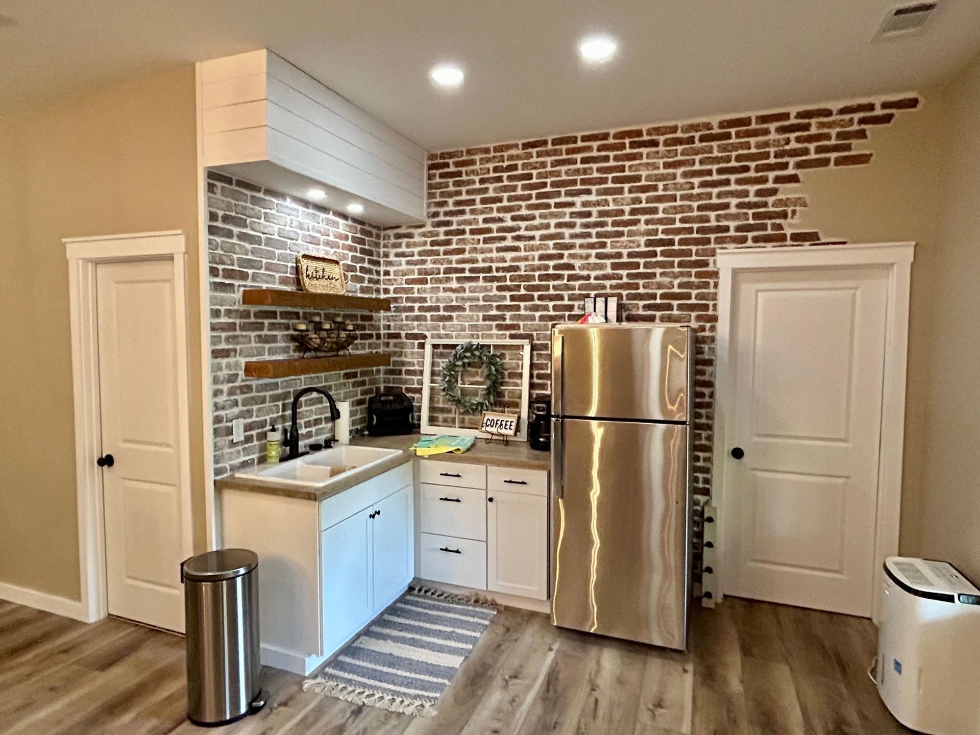 A kitchen with a stainless steel refrigerator , sink , and brick wall.