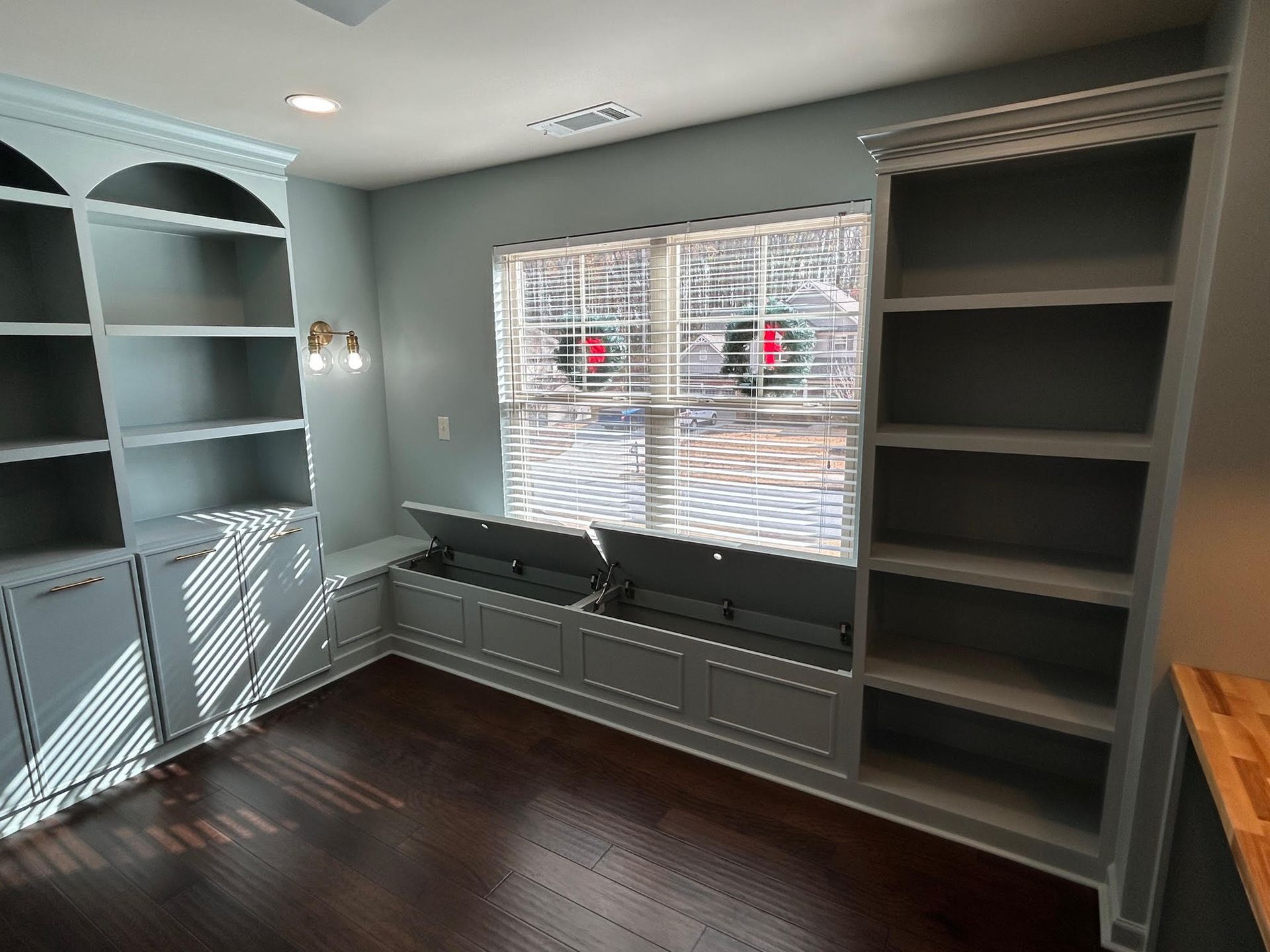 A room with lots of shelves and a window with blinds.