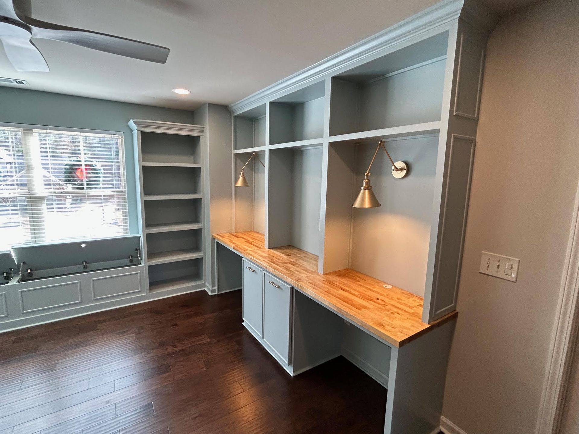 A room with a desk , shelves , and a ceiling fan.