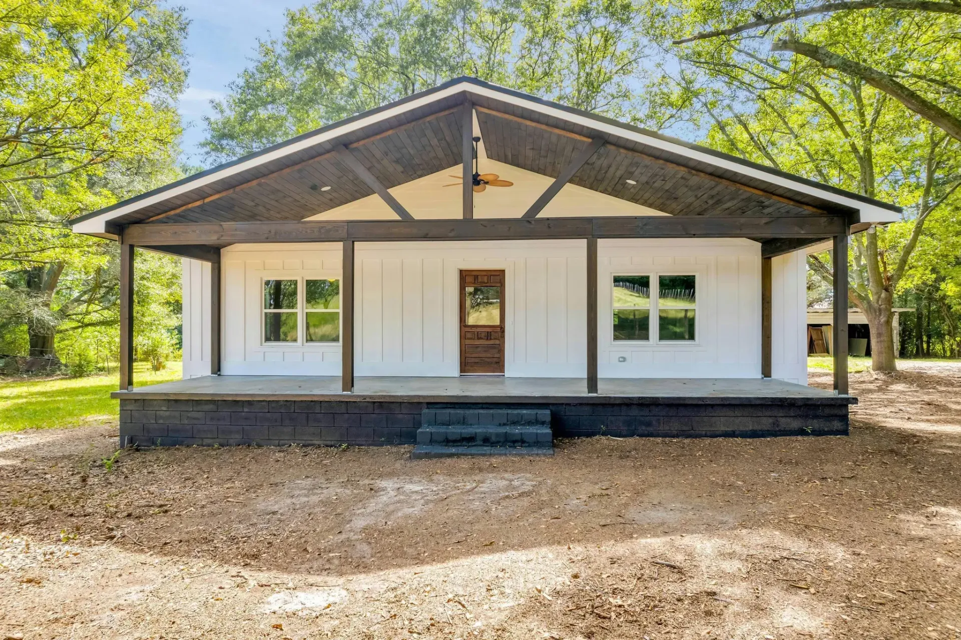 A white house with a porch and trees in the background.