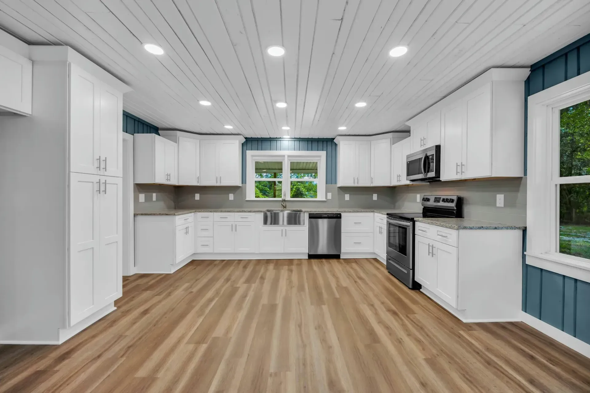 An empty kitchen with white cabinets and hardwood floors.