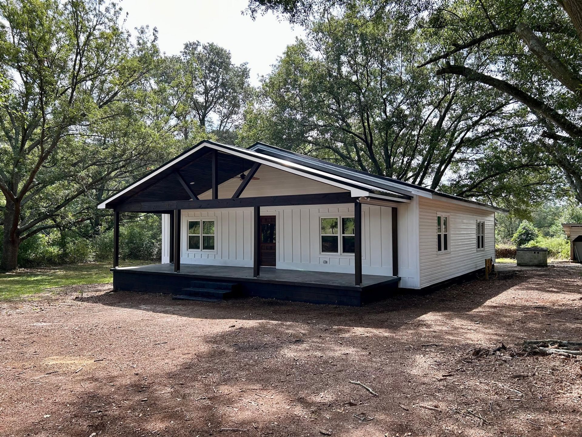 A small white house with a porch and trees in the background.