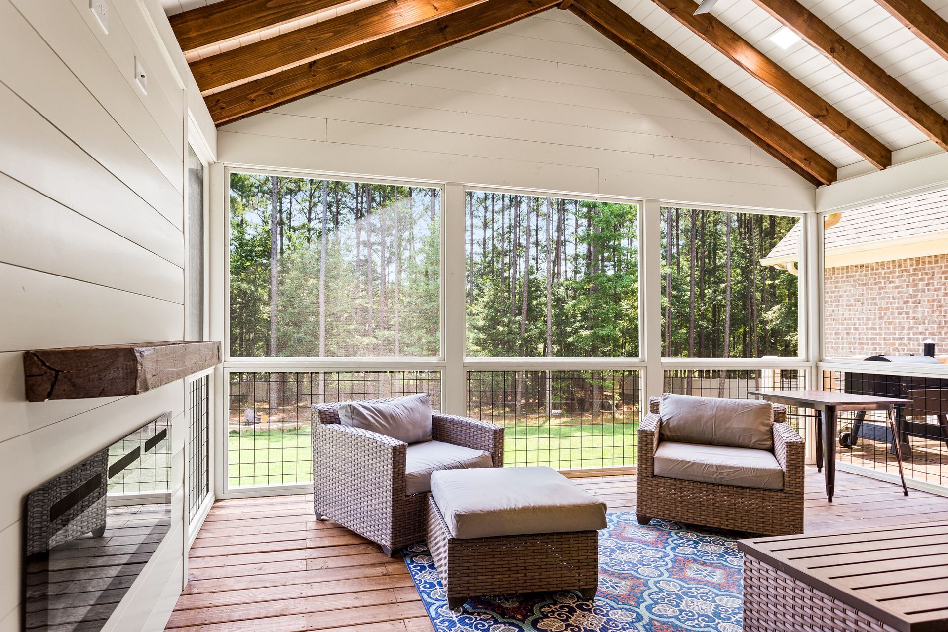 Screened-in porch with wicker furniture, a fireplace, and view of a green backyard.
