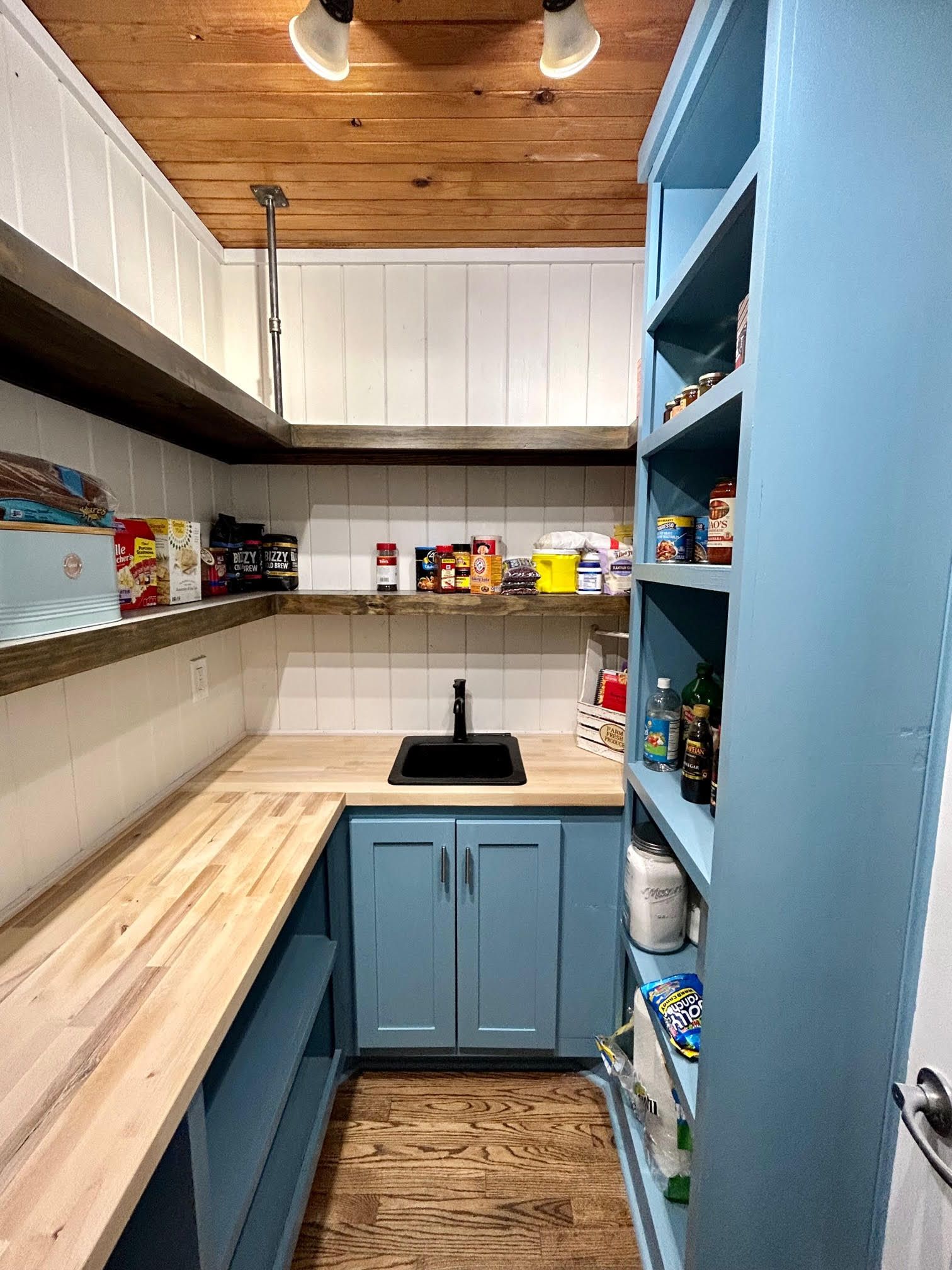 A pantry with blue cabinets and wooden shelves and a sink.