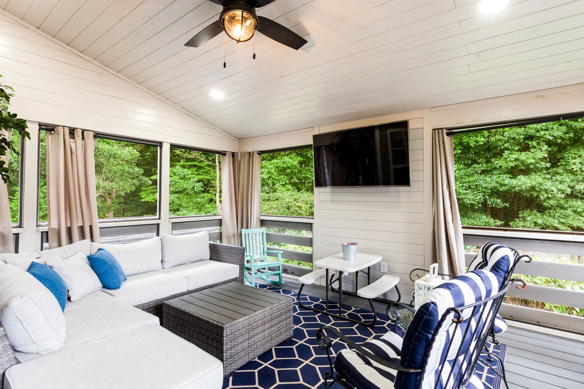 A screened in porch with a couch , chairs , table and television.