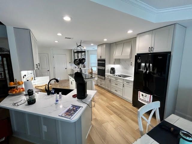 A kitchen with white cabinets and a black refrigerator.