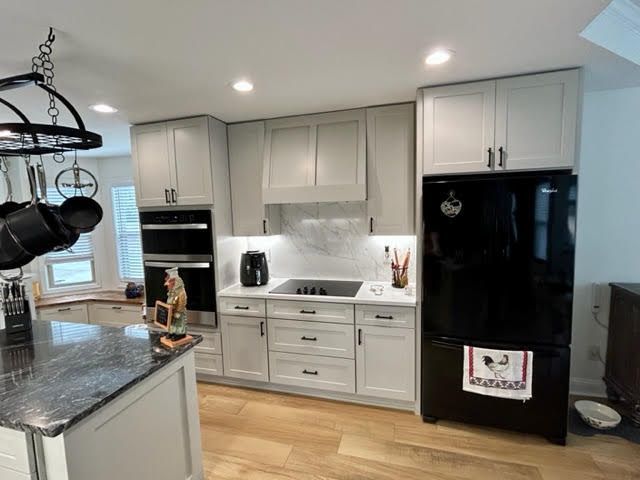 A kitchen with white cabinets and a black refrigerator