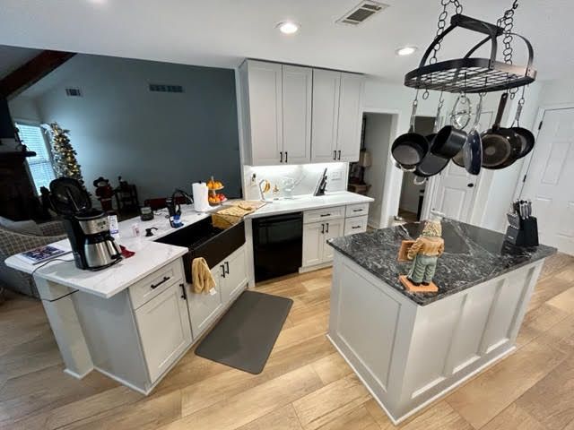 A kitchen with white cabinets and a large island with pots and pans hanging from the ceiling.