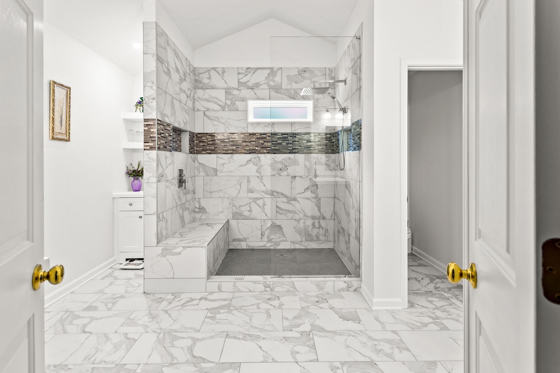 Spacious bathroom with marble tile shower and floors. Includes a bench and glass door.