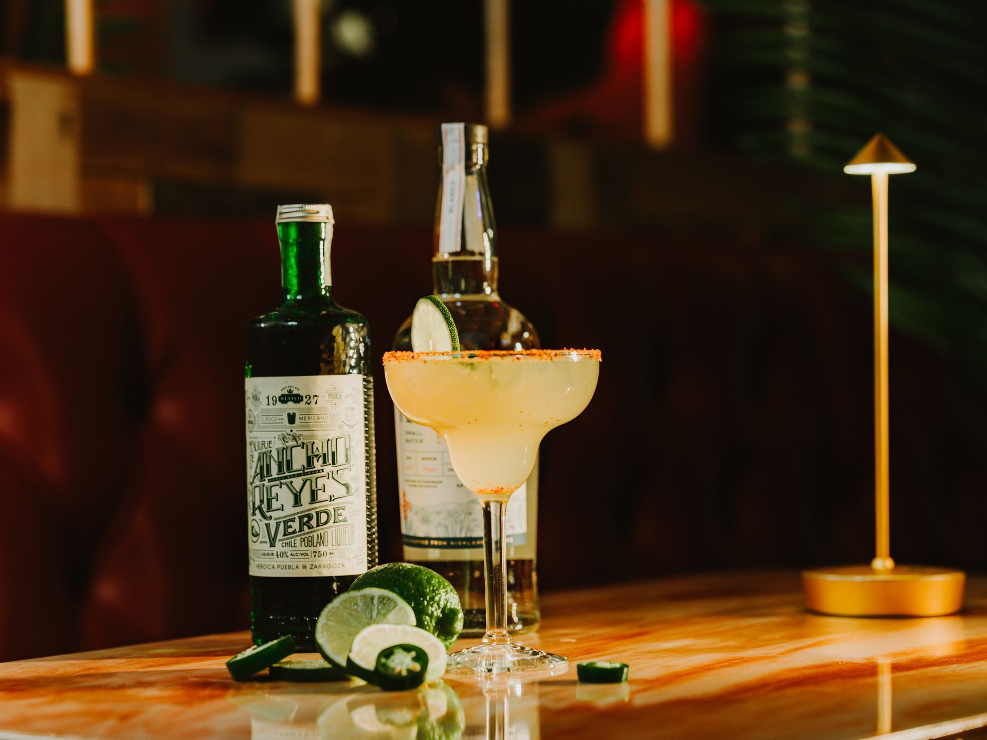 Cocktail and wine bottle on a wooden bar with lime slices and a cocktail umbrella