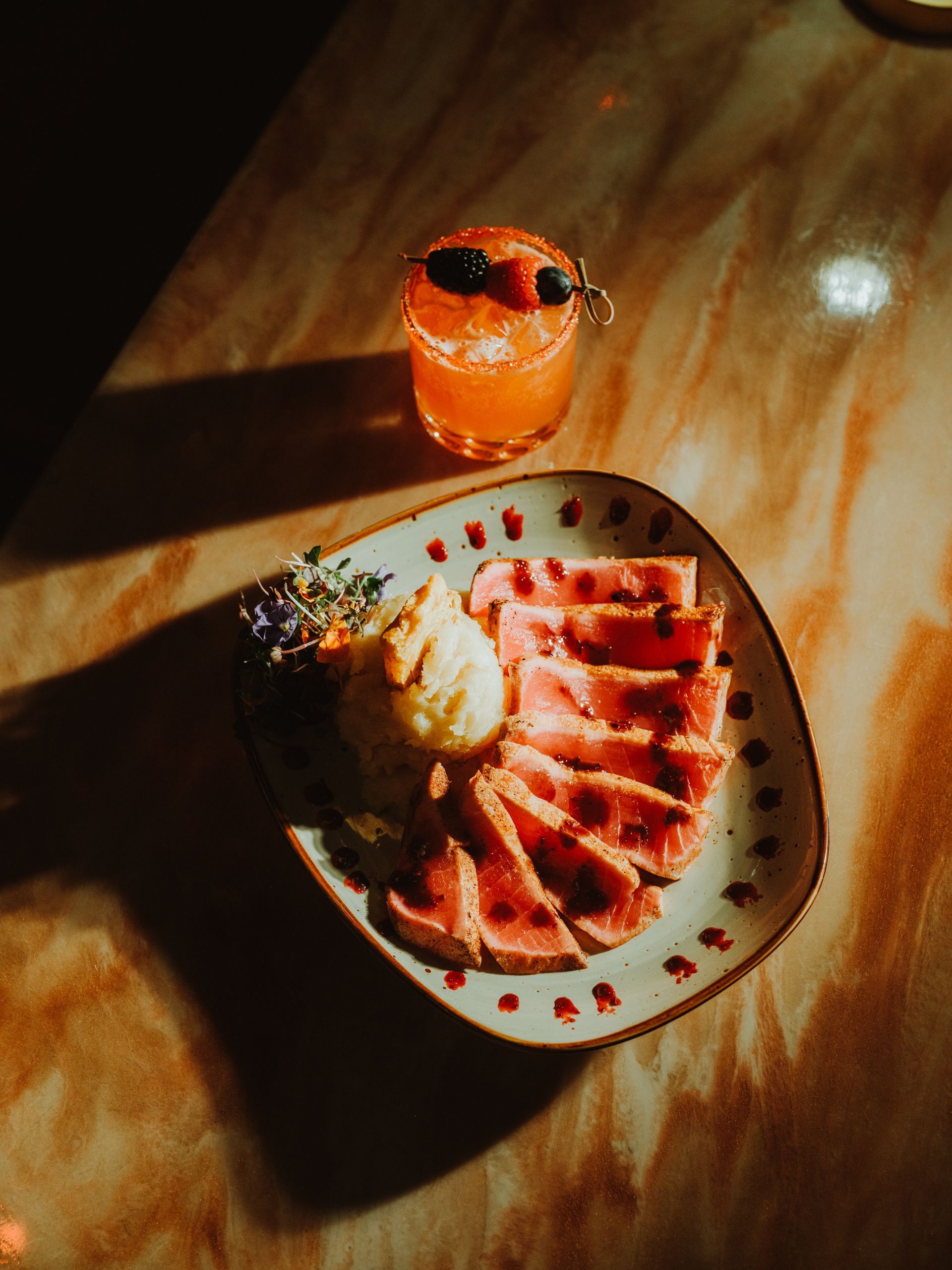 Dessert plate with sliced cake, whipped cream, and a small orange drink on a sunlit table