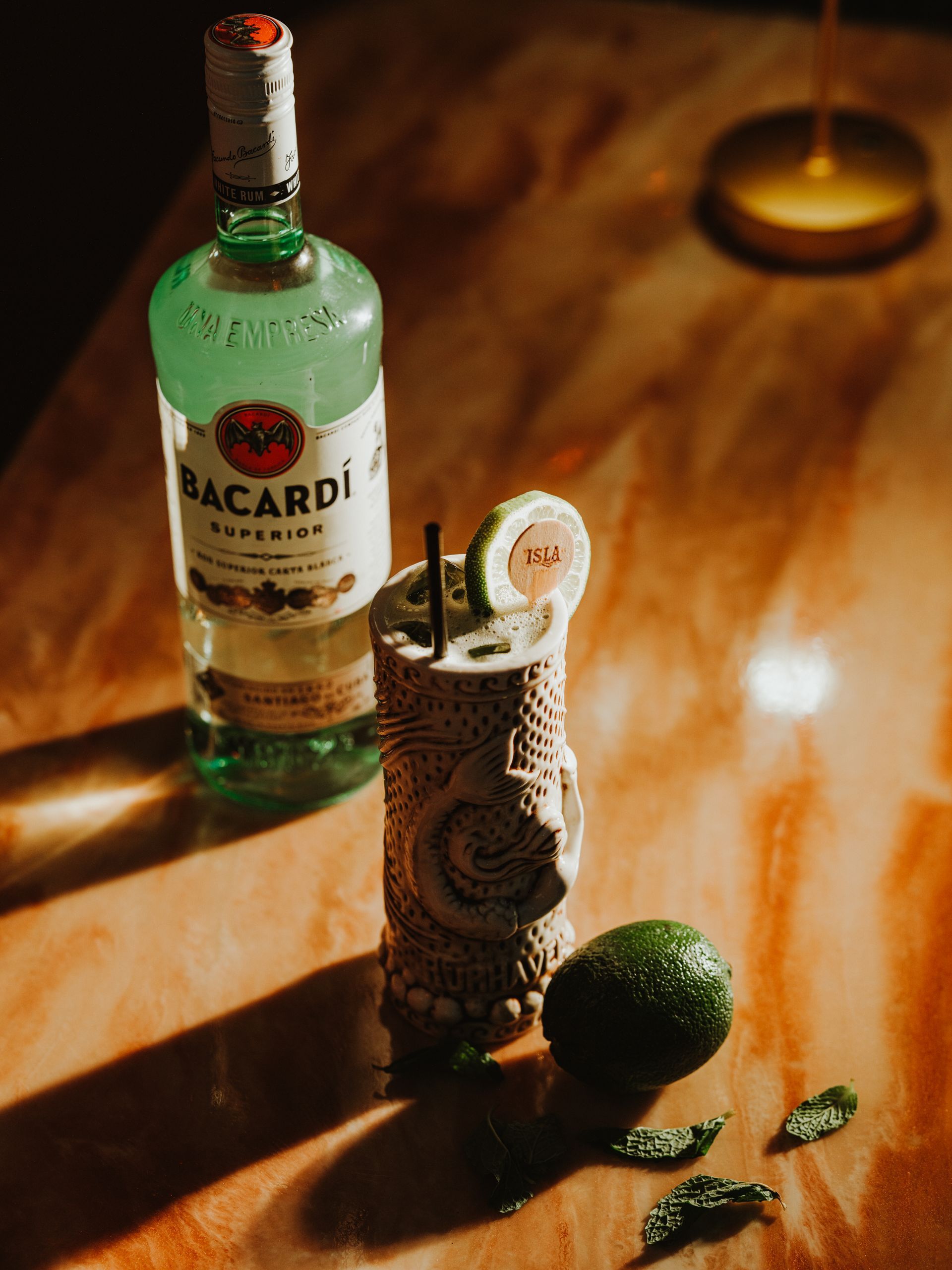 Bacardi rum bottle, tiki cocktail, lime, and garnish on a wooden table with candlelight