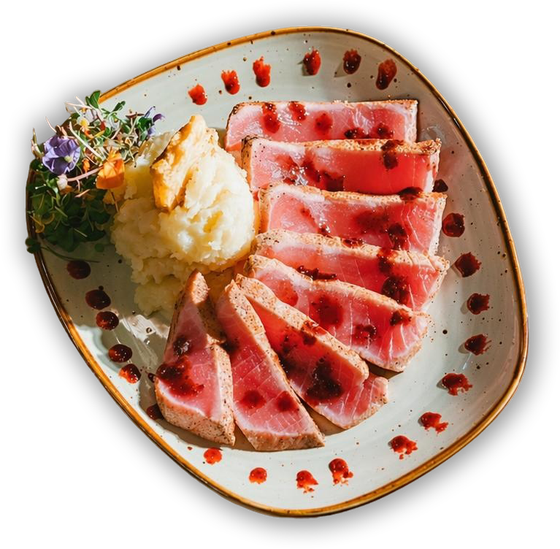 Sliced seared tuna with mashed potatoes and microgreens on a white plate with red sauce dots