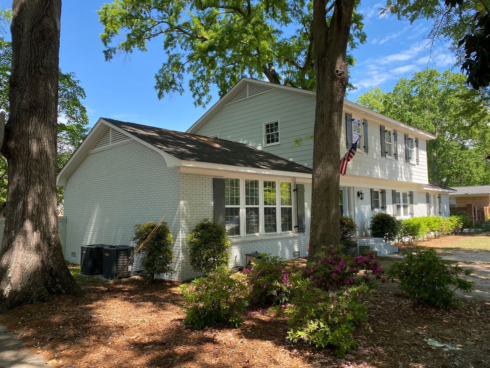 A white house is surrounded by trees and bushes on a sunny day