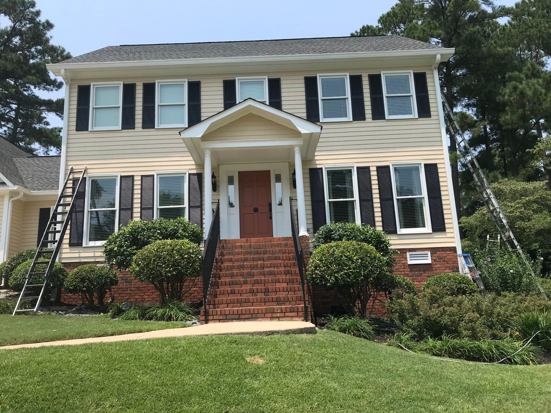 A large house with stairs leading up to the front door is being painted.