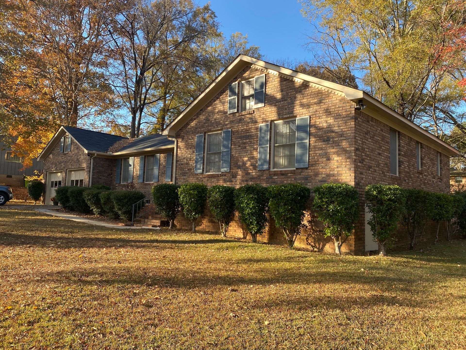 A brick house with blue shutters and bushes in front of it