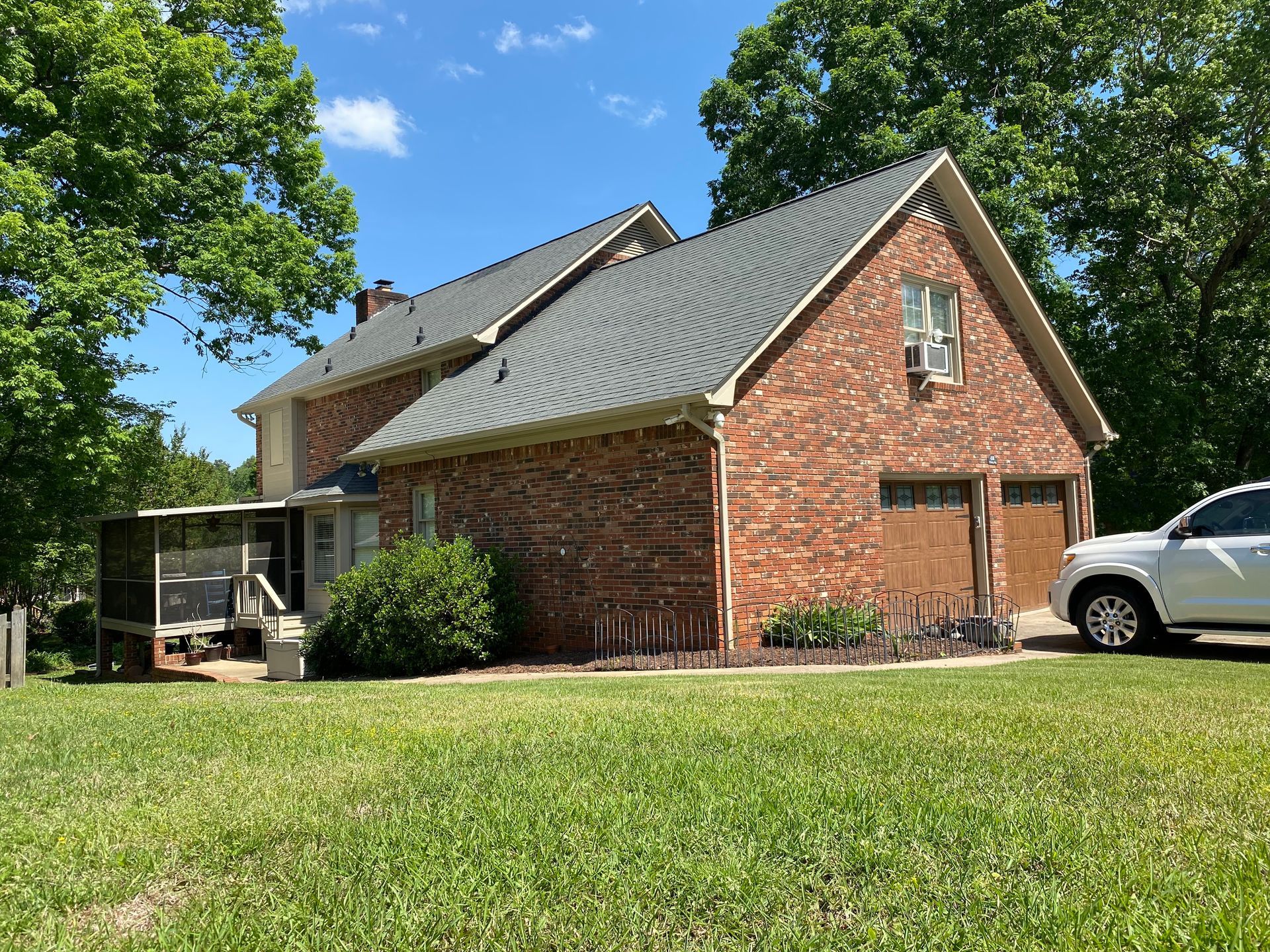 A white car is parked in front of a brick house.