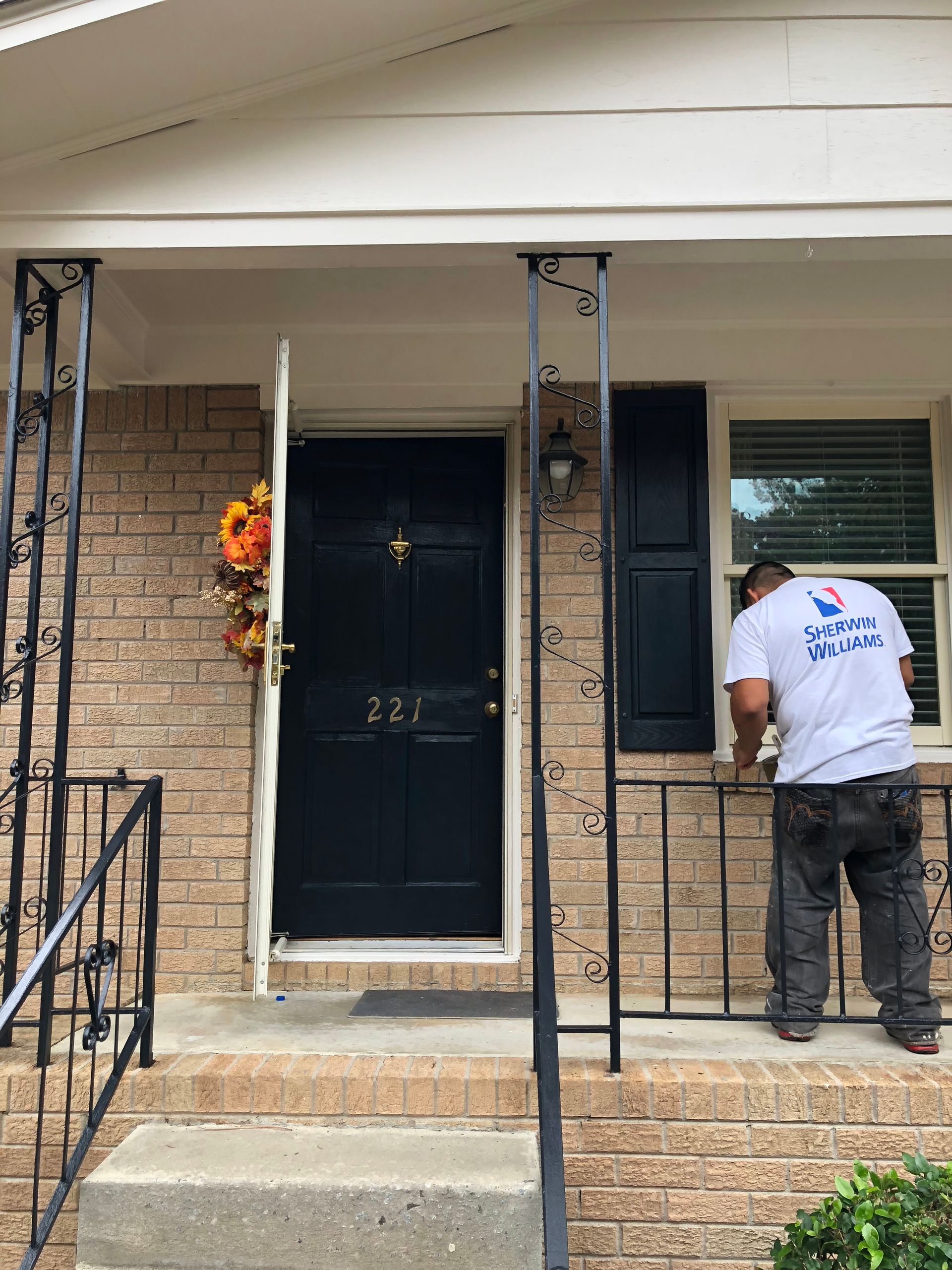 A man in a white shirt is standing on the porch of a house.