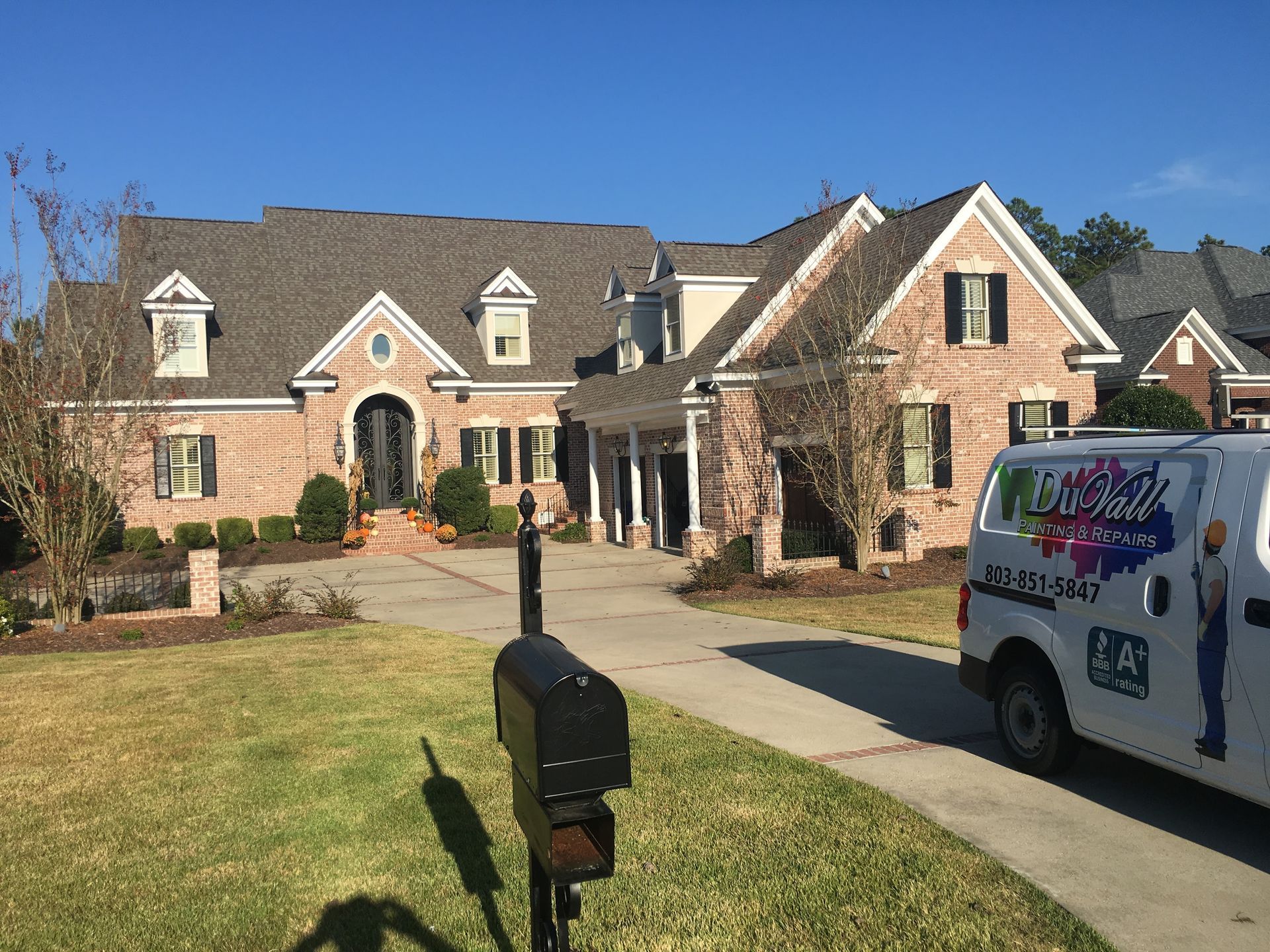 A white van is parked in front of a large brick house.