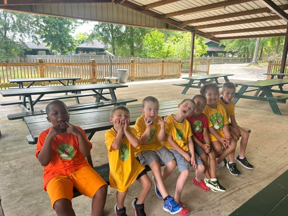 A group of children are sitting on picnic tables under a covered area.