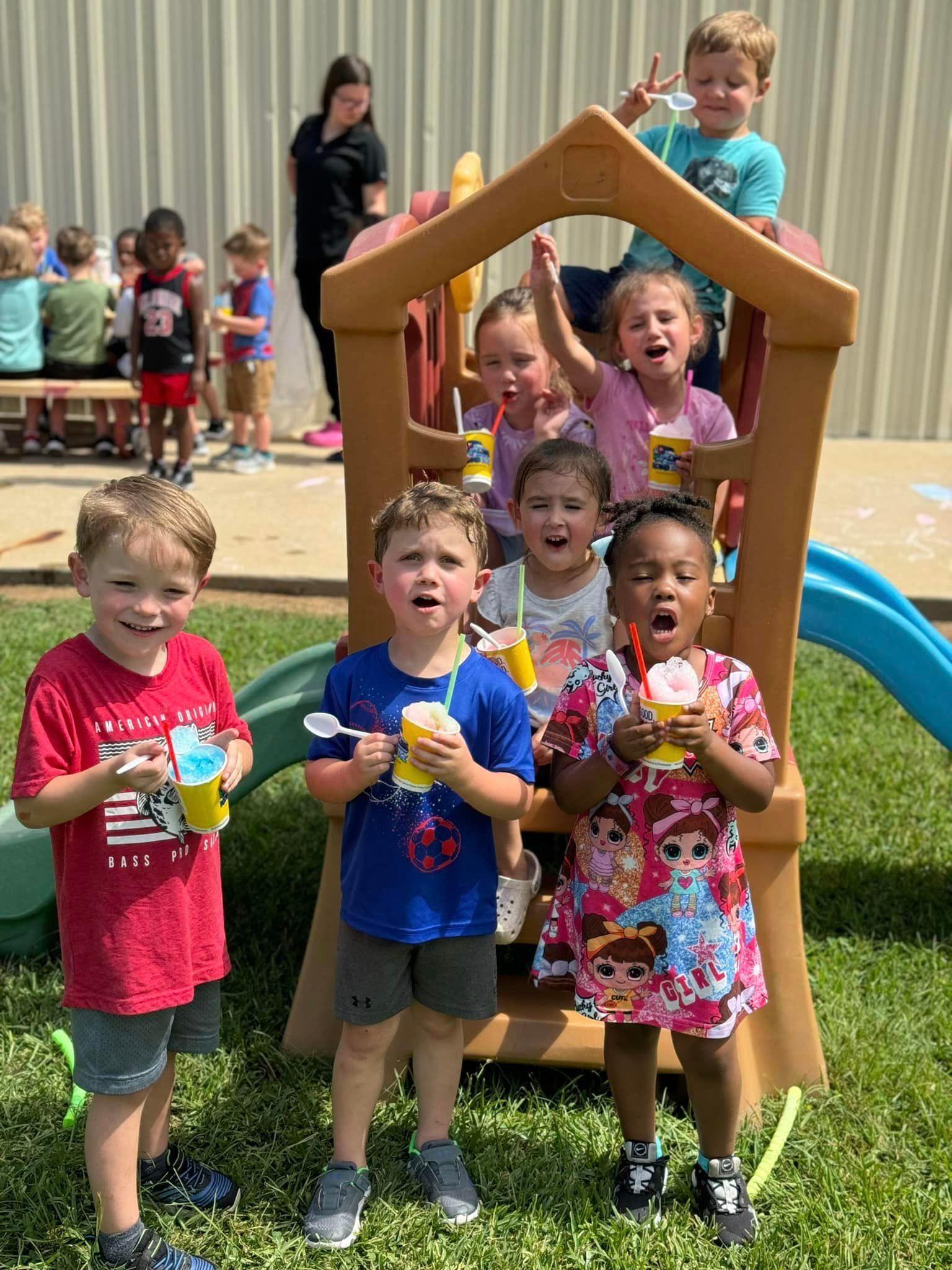 A group of children are standing in front of a playhouse eating ice cream.
