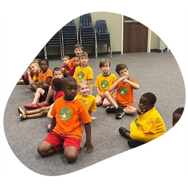 A group of children are sitting on the floor wearing orange and yellow shirts