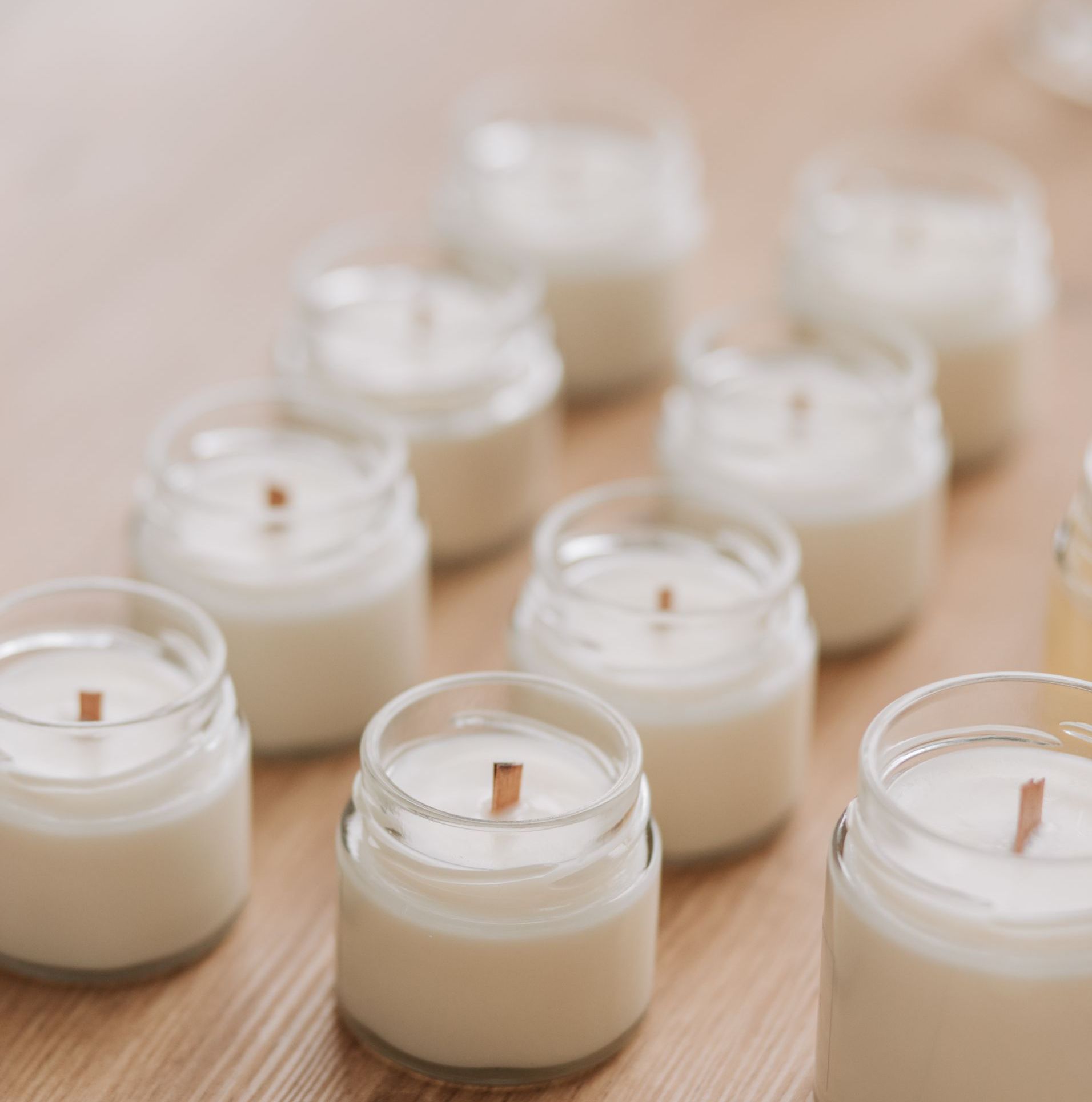 Small glass jar candles with wooden wicks, arranged on a wooden surface.