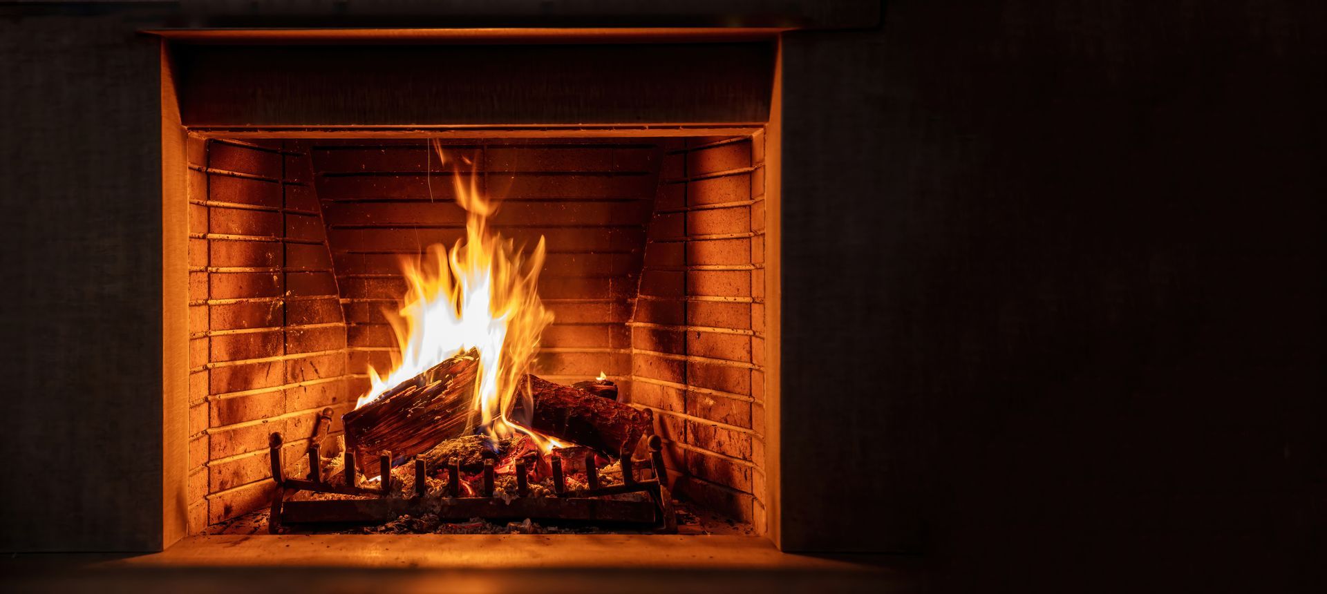Fireplace with burning logs, emitting orange light in a dark room.